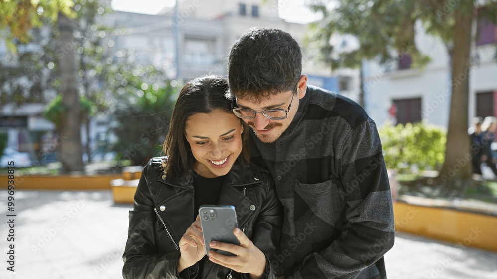 A young couple engaged in viewing a smartphone together on a sunny city street. A young couple engaged in viewing a smartphone together on a sunny city street.