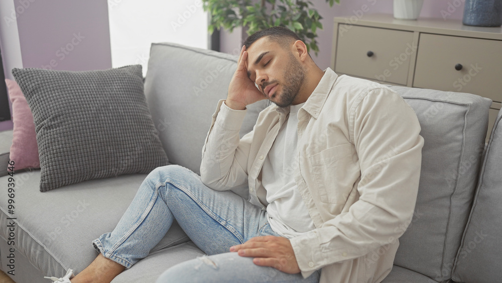 A tired young hispanic man in casual wear resting on a gray sofa in a cozy living room A tired young hispanic man in casual wear resting on a gray sofa in a cozy living room