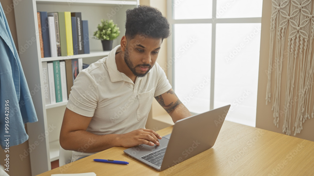 Focused african man working on laptop at home, showcasing casual lifestyle and remote work. Focused african man working on laptop at home, showcasing casual lifestyle and remote work.