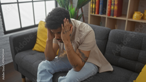 African american man in casual clothing looking stressed and sitting on a couch indoors.