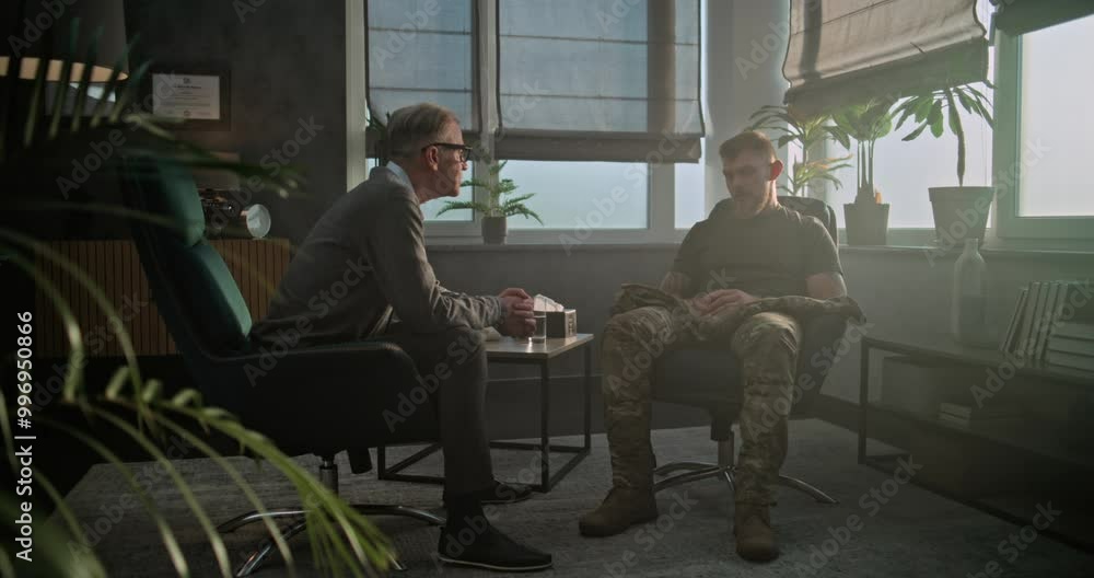 Military man discusses progress in therapy, shakes hands with psychotherapist and leaves after successful rehabilitation. Senior psychologist says goodbye to soldier, smiles while sitting in chair. Military man discusses progress in therapy, shakes hands with psychotherapist and leaves after successful rehabilitation. Senior psychologist says goodbye to soldier, smiles while sitting in chair.