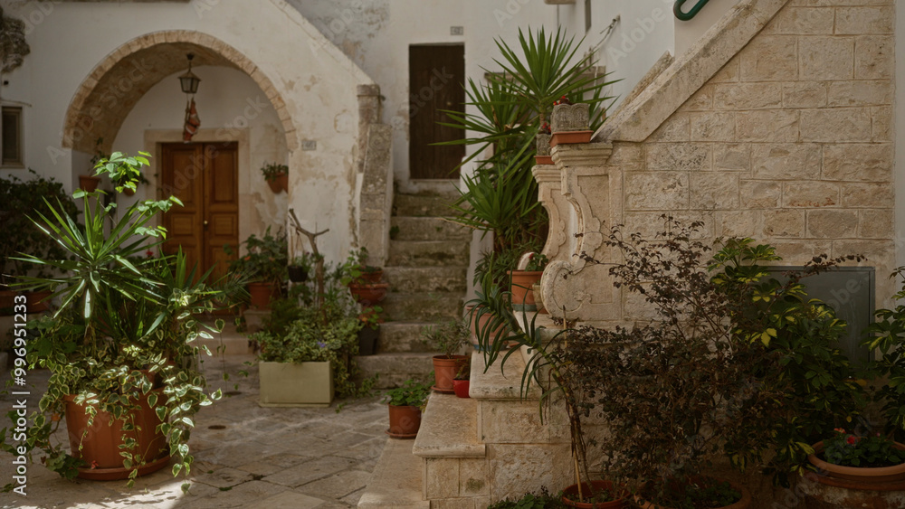 Naklejka premium A charming courtyard filled with potted plants and historic stone architecture in locorotondo, italy, showcasing mediterranean beauty and rustic charm under the puglian sun.