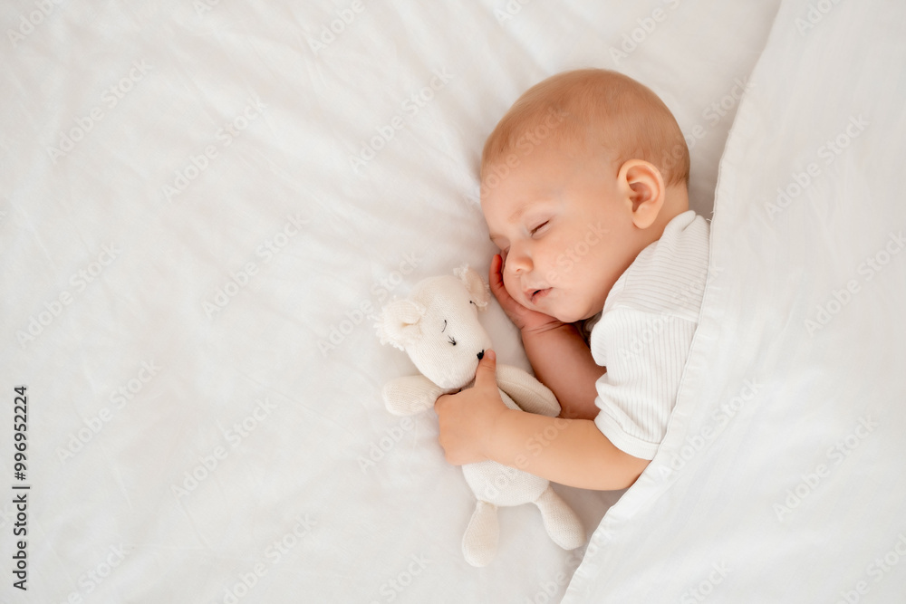 a newborn baby sleeps sweetly holding a toy in his hands, a place for text, a baby sleeps on a white bed under a blanket with a pen under his cheek, a healthy baby's sleep a newborn baby sleeps sweetly holding a toy in his hands, a place for text, a baby sleeps on a white bed under a blanket with a pen under his cheek, a healthy baby's sleep