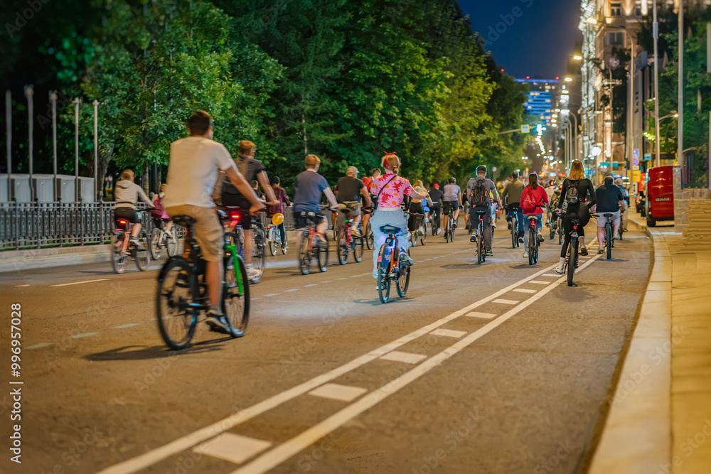 Fototapeta premium People cycling together at night along city street