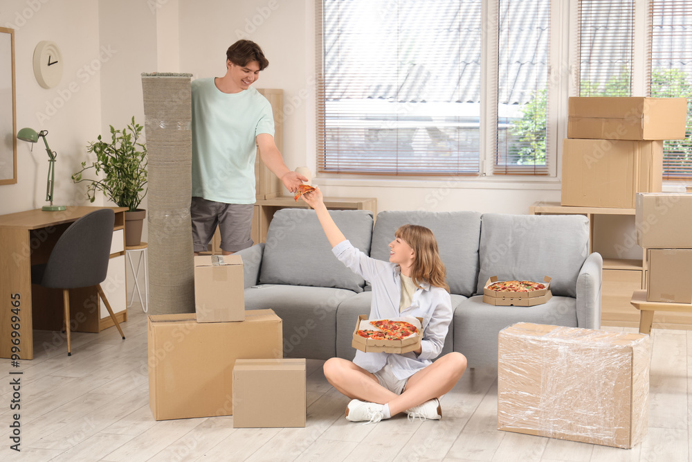 Beautiful young couple with piece of tasty pizza in living room on moving day Beautiful young couple with piece of tasty pizza in living room on moving day