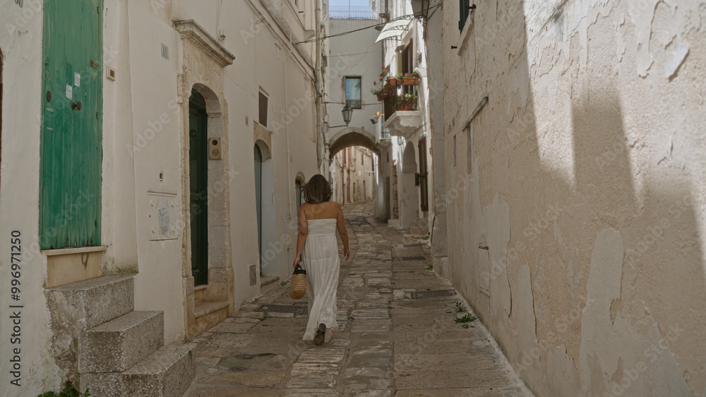 Young hispanic woman in a white dress walking through the old town streets of ostuni, puglia, italy, with a rustic wall and green door in the background. Young hispanic woman in a white dress walking through the old town streets of ostuni, puglia, italy, with a rustic wall and green door in the background.