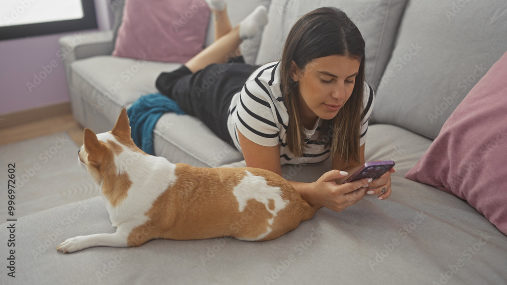 © Krakenimages.com - A woman lies on a sofa using a smartphone with a chihuahua dog beside her in a cozy living room.
