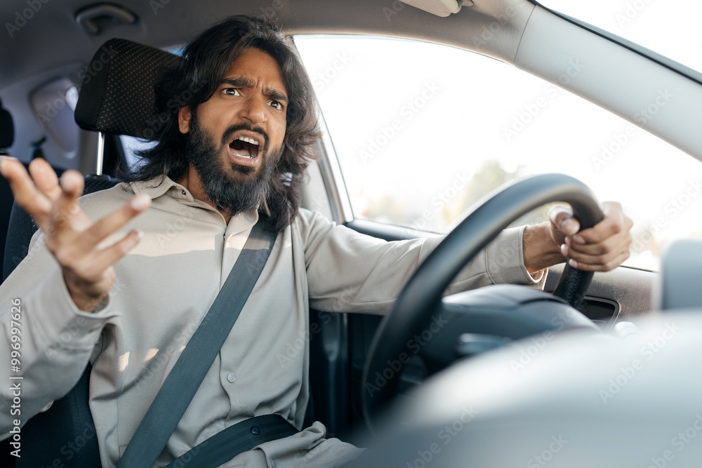 A young Middle eastern man with curly hair exhibits pain or discomfort by holding his head with both hands against a plain background. His expression conveys distress. A young Middle eastern man with curly hair exhibits pain or discomfort by holding his head with both hands against a plain background. His expression conveys distress.