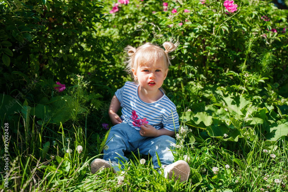 Little toddler child girl walks in a blooming green garden in summer. Little toddler child girl walks in a blooming green garden in summer.
