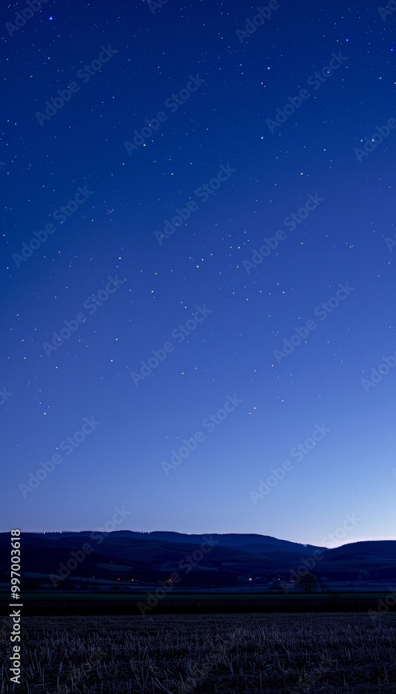 A serene night sky filled with stars above a field and a line of hills in the distance. A serene night sky filled with stars above a field and a line of hills in the distance.