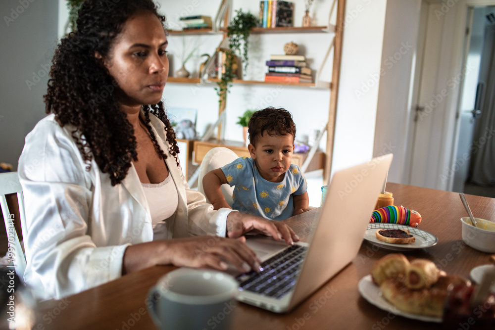 Mother working on laptop while watching toddler son at home Mother working on laptop while watching toddler son at home