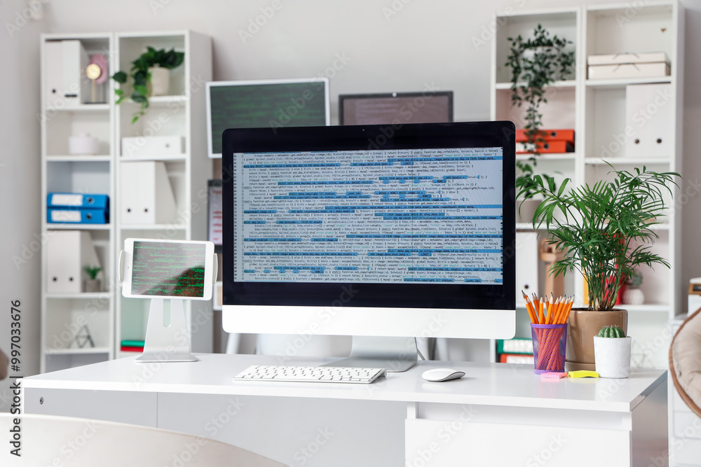 Computer monitor with code and plants on programmer's desk in office Computer monitor with code and plants on programmer's desk in office