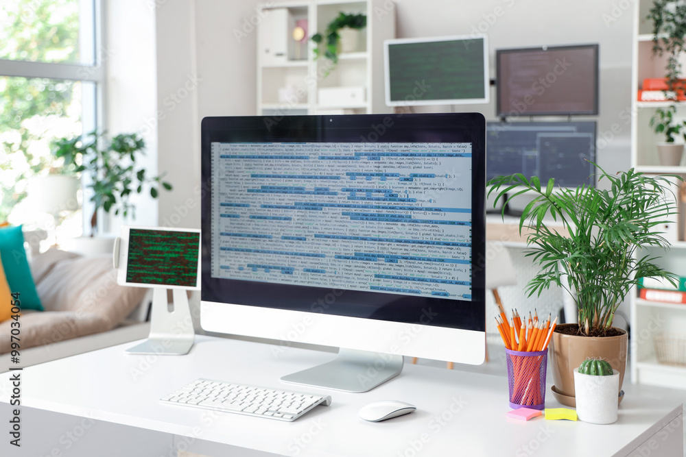Computer monitor with code and plants on programmer's desk in office Computer monitor with code and plants on programmer's desk in office