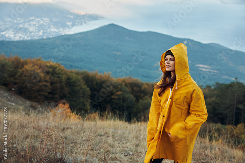 A woman in a yellow raincoat standing on a hill admiring the majestic mountain landscape in the distance