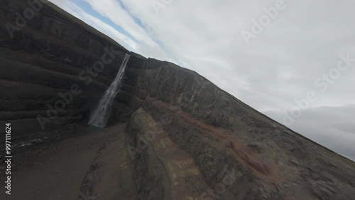 Flying alongside cliffs and diving down the waterfall, capturing vibrant, cinematic views of this stunning natural wonder of Hengifoss waterfall in Iceland. D-log unedited footage. photo