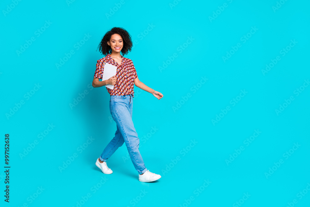 Full length photo of positive busy girl wear print shirt holding tablet walk at work to empty space isolated on blue color background Full length photo of positive busy girl wear print shirt holding tablet walk at work to empty space isolated on blue color background