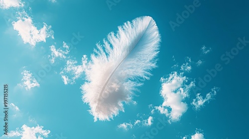 A single white feather floats gently against a bright blue sky with puffy white clouds. photo