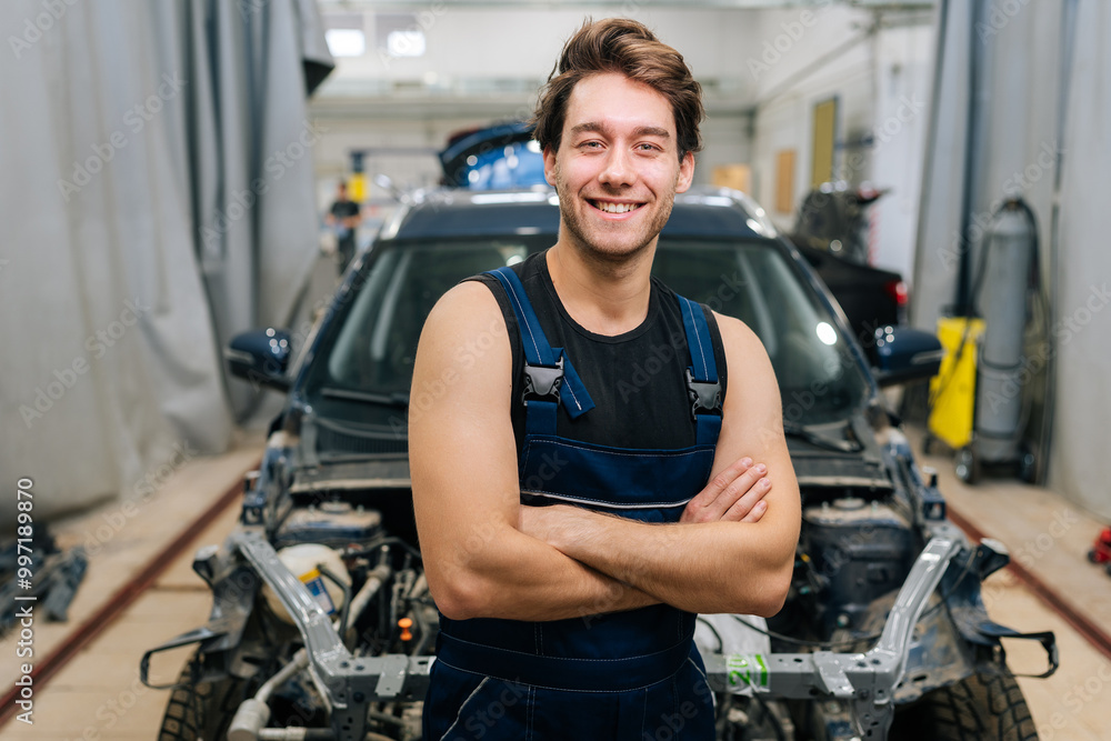Portrait of friendly male mechanic wearing uniform smiling looking camera standing posing with crossed hands in auto service shop. Concept of professional automobile maintenance. Portrait of friendly male mechanic wearing uniform smiling looking camera standing posing with crossed hands in auto service shop. Concept of professional automobile maintenance.