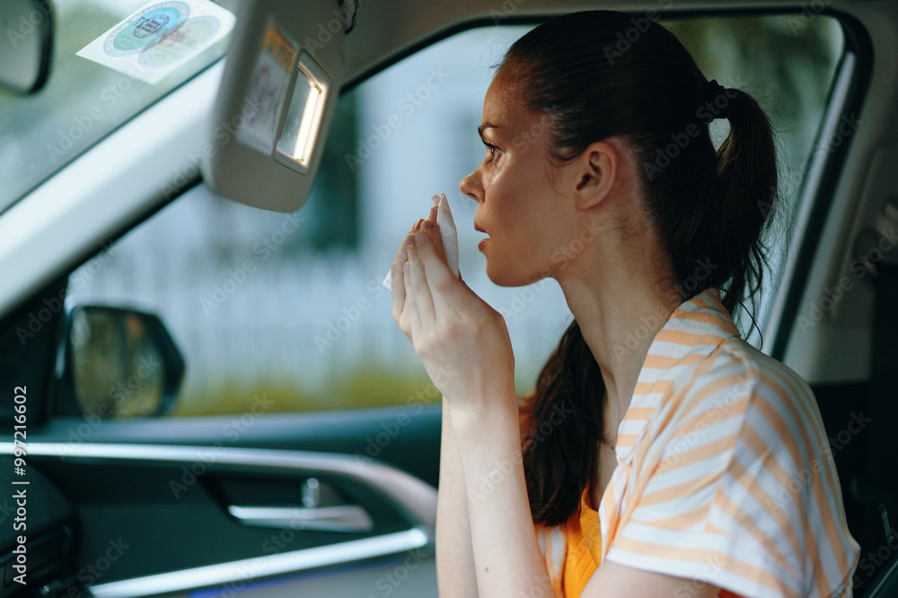 Naklejka premium woman applying makeup in a car interior, soft light, natural expression, casual outfit, focused on reflection, urban background, vibrant colors, beauty routine, self care moments, self confidence