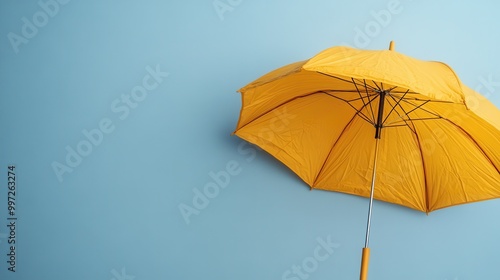 A brightly colored yellow umbrella is displayed against a pastel light blue backdrop, creating a contrast that is both striking and aesthetically pleasing. photo