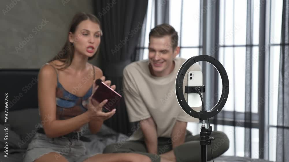 Young woman making beauty and cosmetic tutorial video content for social media using her boyfriend as model and light ring. Beauty blogger showing how to beauty care to audience or follower. Adit Young woman making beauty and cosmetic tutorial video content for social media using her boyfriend as model and light ring. Beauty blogger showing how to beauty care to audience or follower. Adit