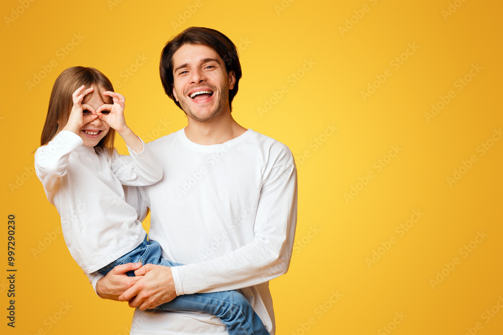 Naklejka premium Funny little daughter and daddy fooling, having fun over yellow background, girl imitating binoculars