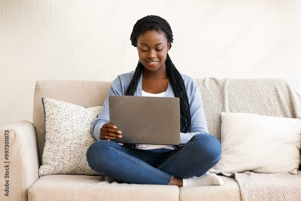 Naklejka premium Freelance concept. African american millennial woman working with laptop computer on sofa at home