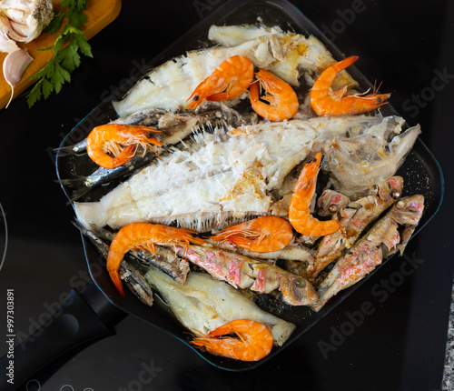 Preparation of delicious seafood meal. Variety of shrimp, red mullet, sardines and sole fish, sizzling in hot pan on stovetop photo