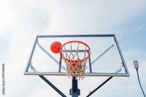 Basketball Swishes Through Hoop at Vibrant Outdoor Court Under Sunny Sky During Afternoon Game