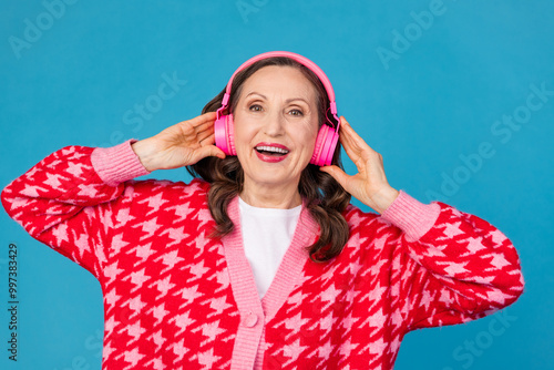 Photo portrait of lovely senior lady touch headphones listen music dressed stylish pink print garment isolated on blue color background photo