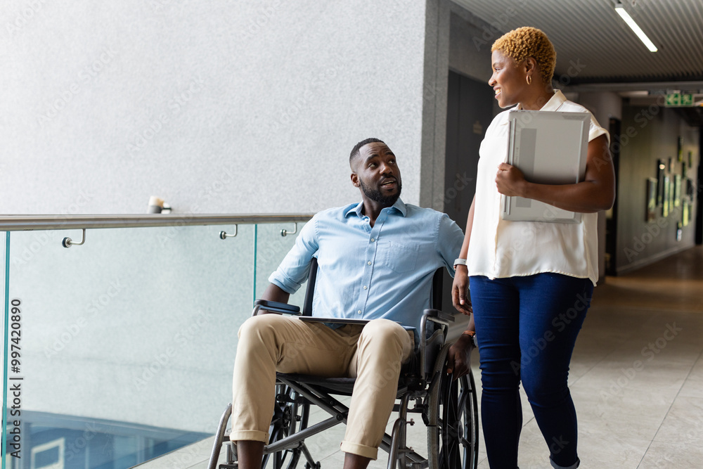Obraz premium Colleagues discussing work, african american man in wheelchair holding tablet, woman carrying laptop