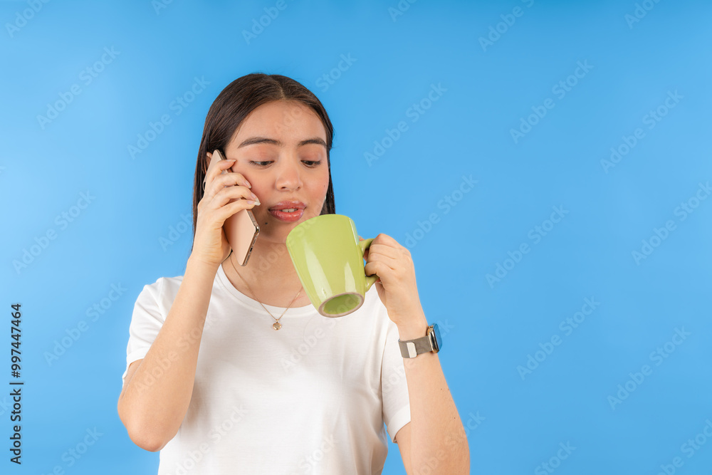 Young latin woman drinking coffee and talking on the phone on blue background Young latin woman drinking coffee and talking on the phone on blue background