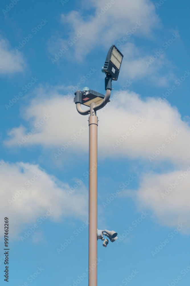 Outdoor floodlight pole for public park with blue sky and white clouds background Outdoor floodlight pole for public park with blue sky and white clouds background