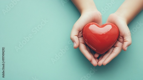 Hands holding a glossy red heart on a teal background.