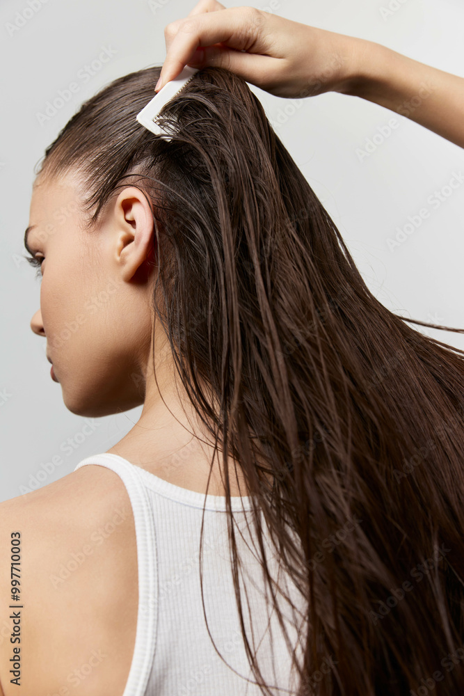 Naklejka premium Hair styling, long hair, grooming, beauty portrait of a woman combing her hair against a plain background showcasing her elegance and effortless style