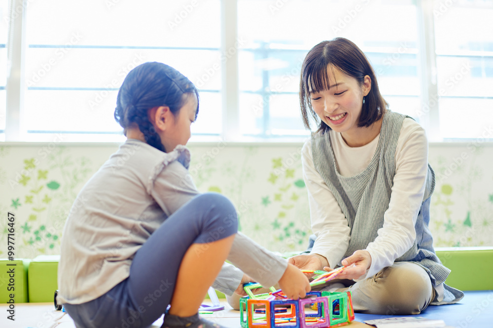 託児所でおもちゃで子供と遊ぶ保育士の女性 託児所でおもちゃで子供と遊ぶ保育士の女性