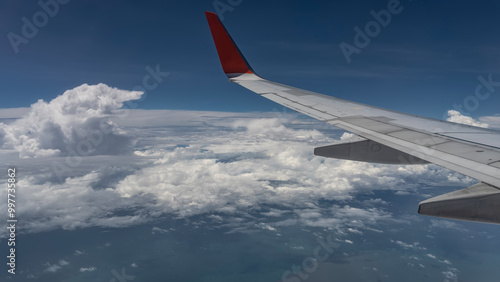 The wing of an airplane flying over the ocean. The background is a blue sky, picturesque fluffy cumulus clouds. Malaysia. 