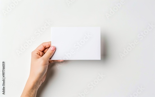 Hand holding a blank white card against a light background. Mockup template for greeting cards and invitations.