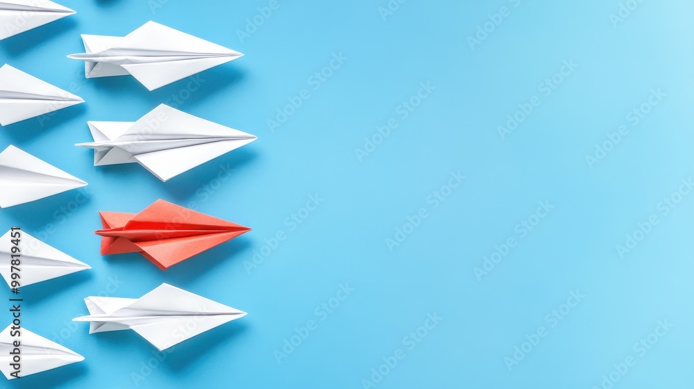 Fototapeta premium A single red paper airplane stands out from a line of white ones on a light blue background.
