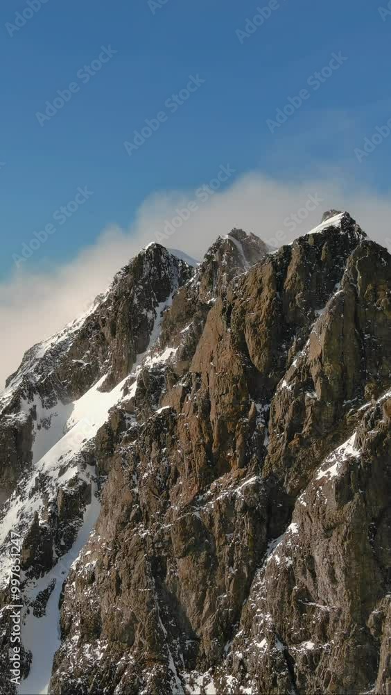 Fast moving clouds over a rocky, snowy mountain peak with blue skies in the background. British Columbia, Canada. Fast moving clouds over a rocky, snowy mountain peak with blue skies in the background. British Columbia, Canada.