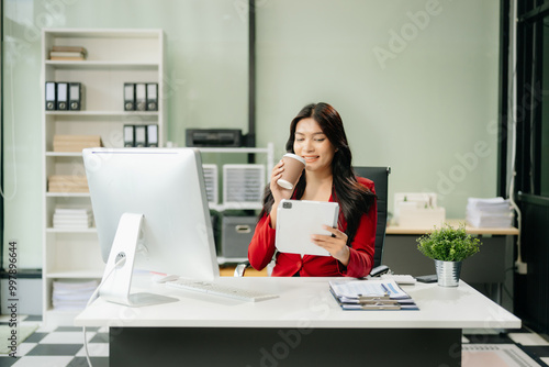 Asian woman using laptop and tablet while sitting at her working place