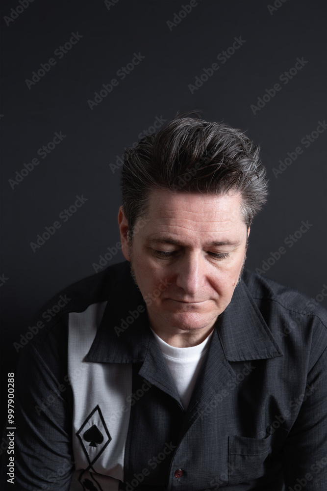 Fototapeta premium Portrait of a sad and sorrowful mature man looking down on dark background. Copy space. Concept of sadness, depression and mental health