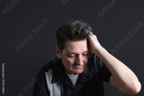 Portrait of a pensive mature man with a lost look and a hand on his nice hair. Dark background. Copy space. Concept of men, maturity and feelings