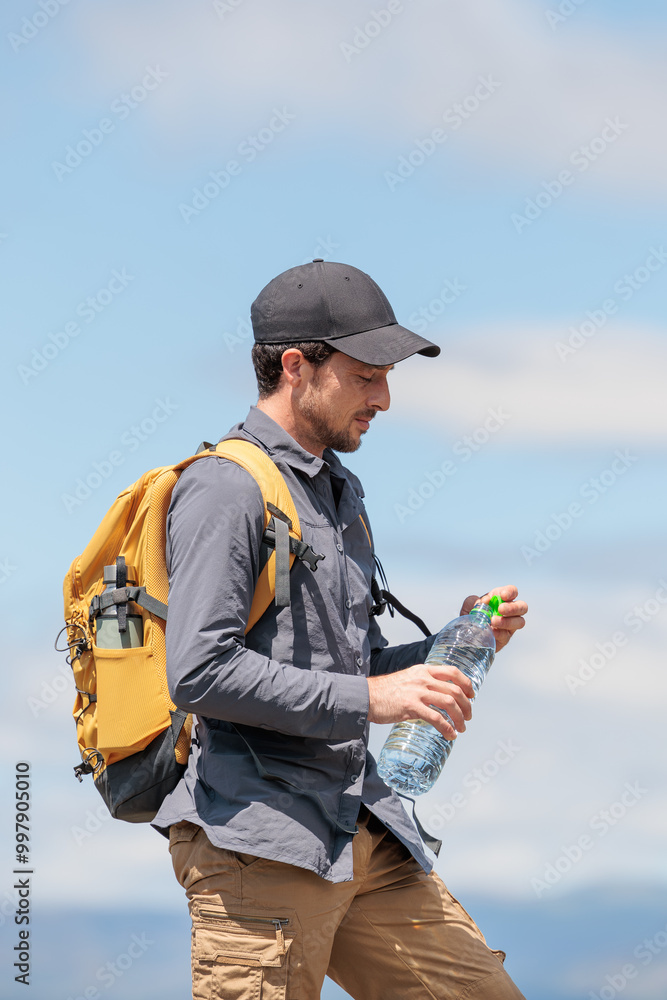 Naklejka premium Young man enjoying nature. Drinking water is very important and healthy. Always stay hydrated. Hiking in the mountains, observing the landscape. Practicing sports and physical activity. Moments