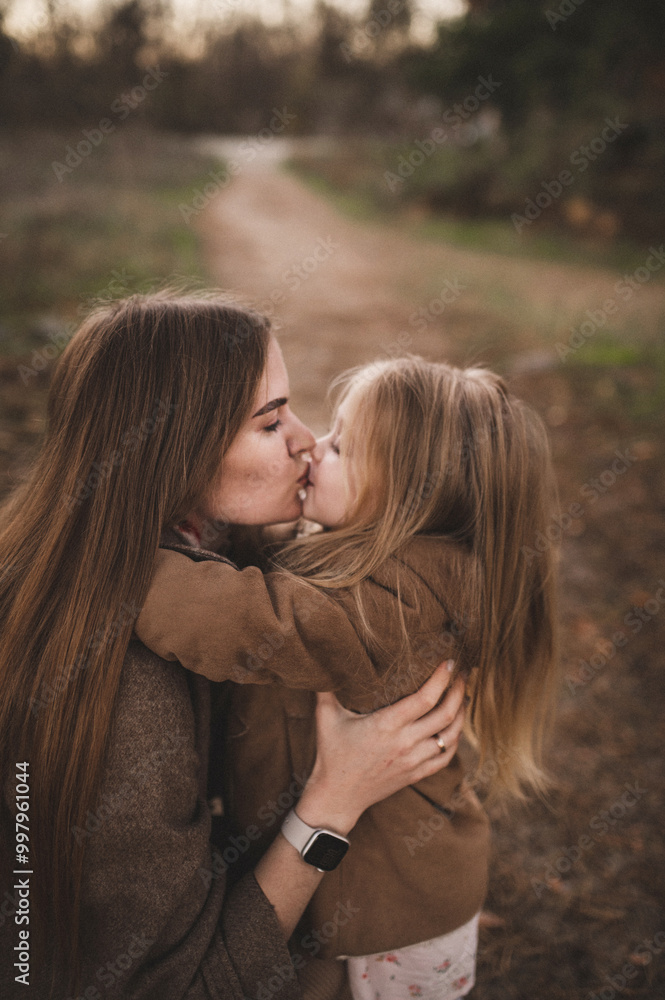 A pregnant woman and her daughter walk through an autumn forest, along the beach near the river in stylish beige coats. Noise blurred toned vintage image A pregnant woman and her daughter walk through an autumn forest, along the beach near the river in stylish beige coats. Noise blurred toned vintage image