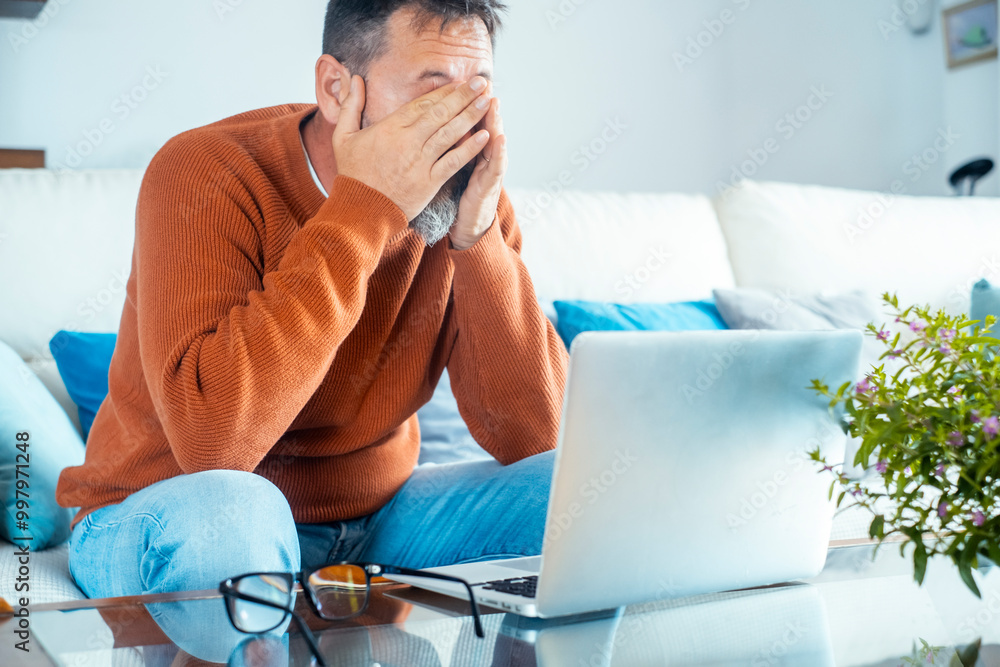 Φωτογραφία An exhausted man sitting on the sofa at home, facing financial problems and reading troubling emails from his lawyer about his divorce and family bankruptcy