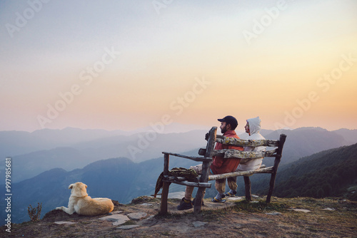 Two men sitting  on a bench chairs enjoy sunset and chatting outdoors at the Top of Raghupur Fort - Tirthan Valley Himanchal  pradesh india.