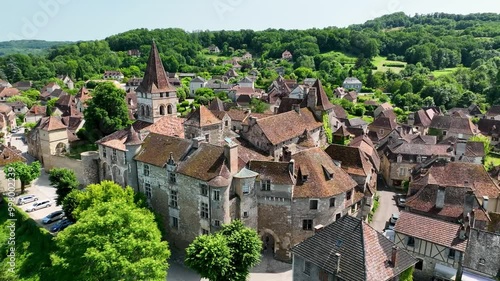 Aerial view of a beautiful village nestled along a peaceful river, with charming stone houses and a historic church surrounded by lush greenery.