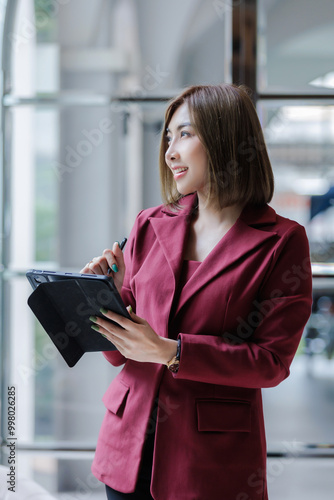 A woman stands using a tablet to work and thinks of ideas.