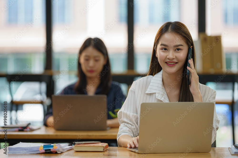 A woman is talking on her cell phone while sitting at a desk with a laptop. A woman is talking on her cell phone while sitting at a desk with a laptop.